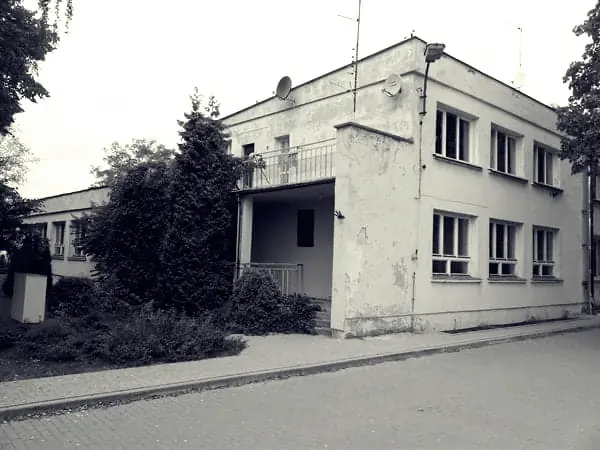 Archiwalne, czarno-białe zdjęcie zniszczonego budynku przed remontem — odpadający tynk, zarośnięte otoczenie.