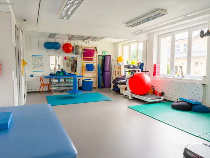 Sala rehabilitacyjna z matami, piłkami, drabinkami i sprzętem do ćwiczeń.