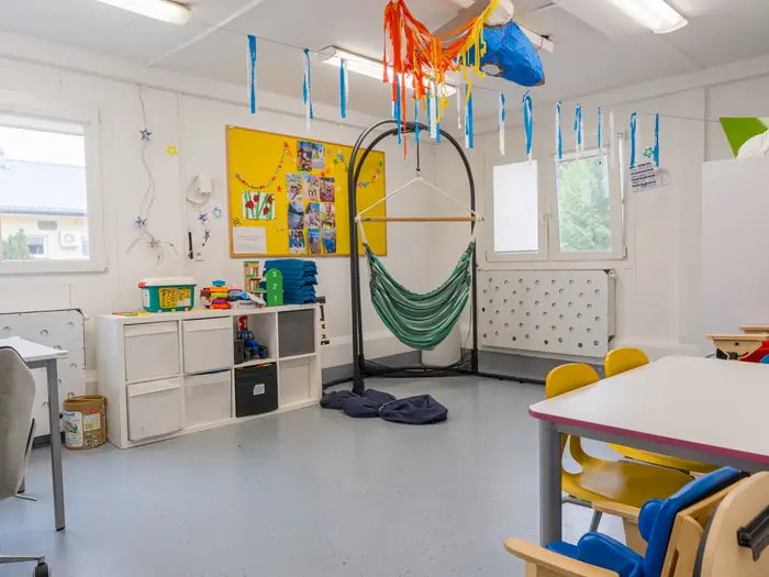 Sala terapeutyczna z hamakiem, krzesełkiem rehabilitacyjnym i stolikiem do pracy.