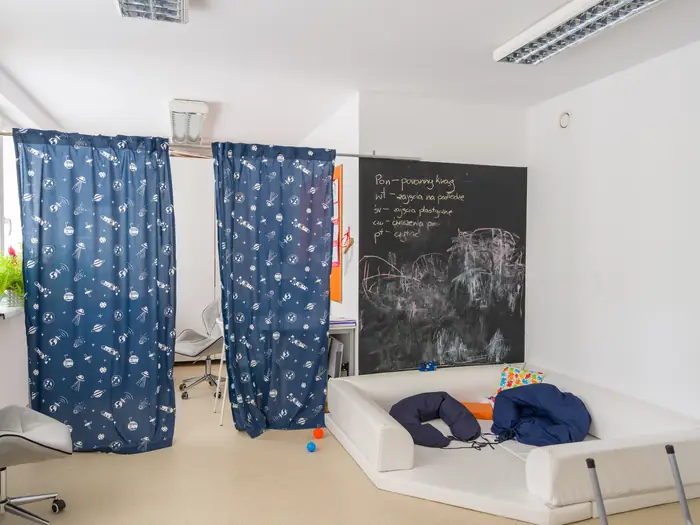 Sala terapeutyczna z materacem, tablicą kredową i zasłonami do wyciszenia.