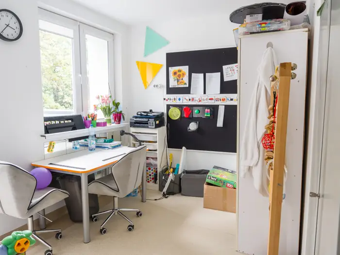 Gabinet terapeutyczny z biurkiem, tablicą i kwiatami w oknie.