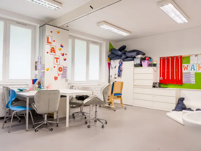 Sala szkolna z biurkami na kółkach i napisem LATO na ścianie.