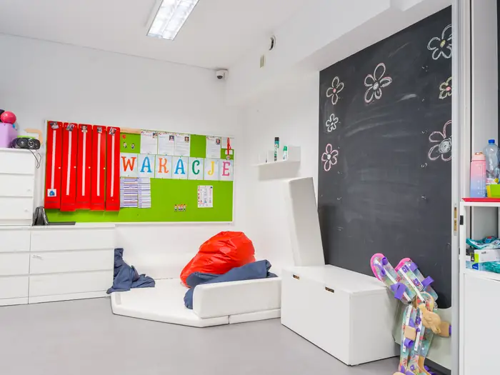 Sala z tablicą kredową, czerwoną kotarą i miękkimi siedziskami.