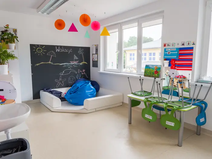 Sala z tablicą kredową, kolorowymi stolikami i materacem do odpoczynku.