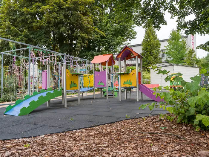 Plac zabaw ze zjeżdżalnią, domkiem i bezpieczną nawierzchnią.