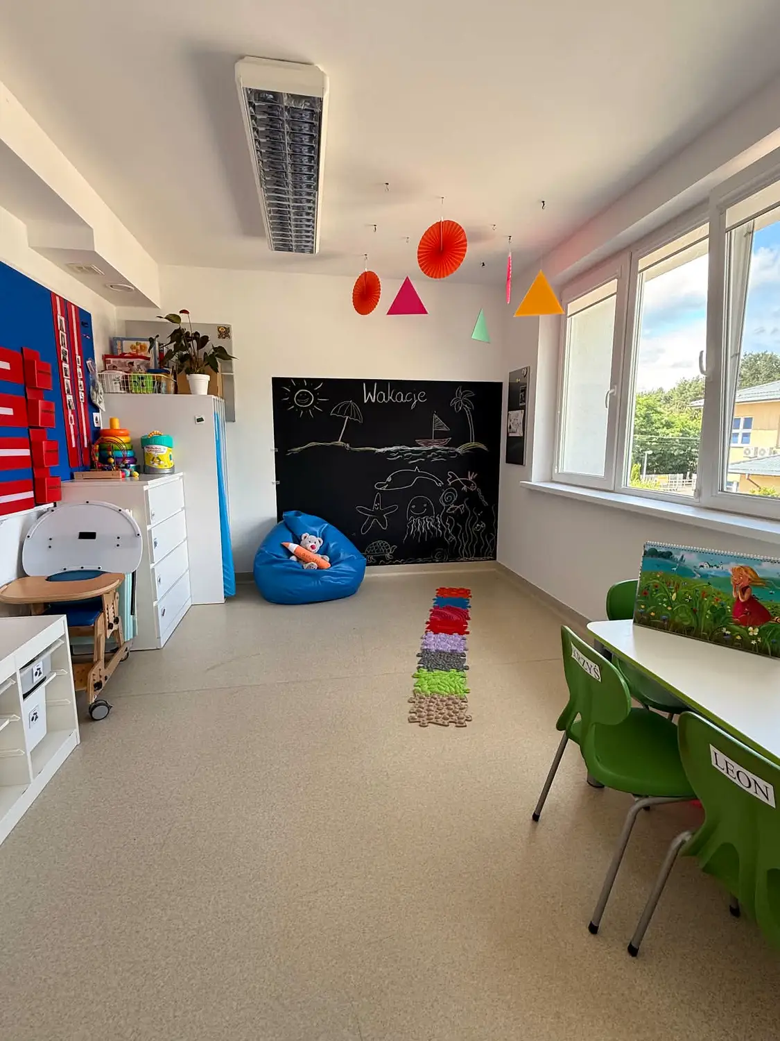 Sala z tablicą kredową, niebieskim workiem sako i sensoryczną ścieżką na podłodze.