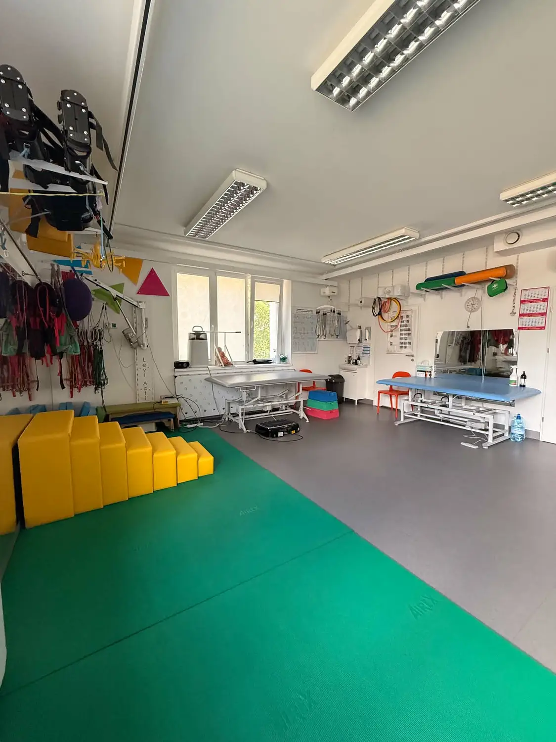 Sala rehabilitacyjna z zieloną matą, drabinkami i pomocami do terapii ruchowej.