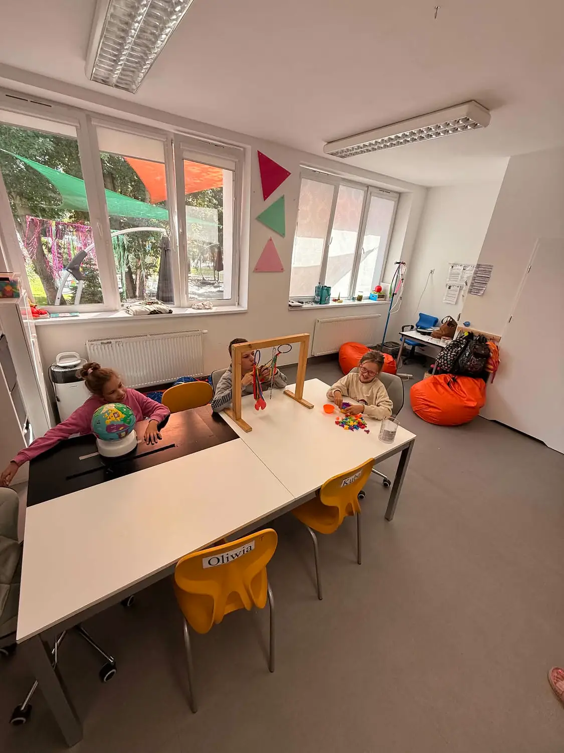 Sala zajęciowa ze wspólnym stołem, żółtymi krzesełkami i miękkimi workami do odpoczynku.