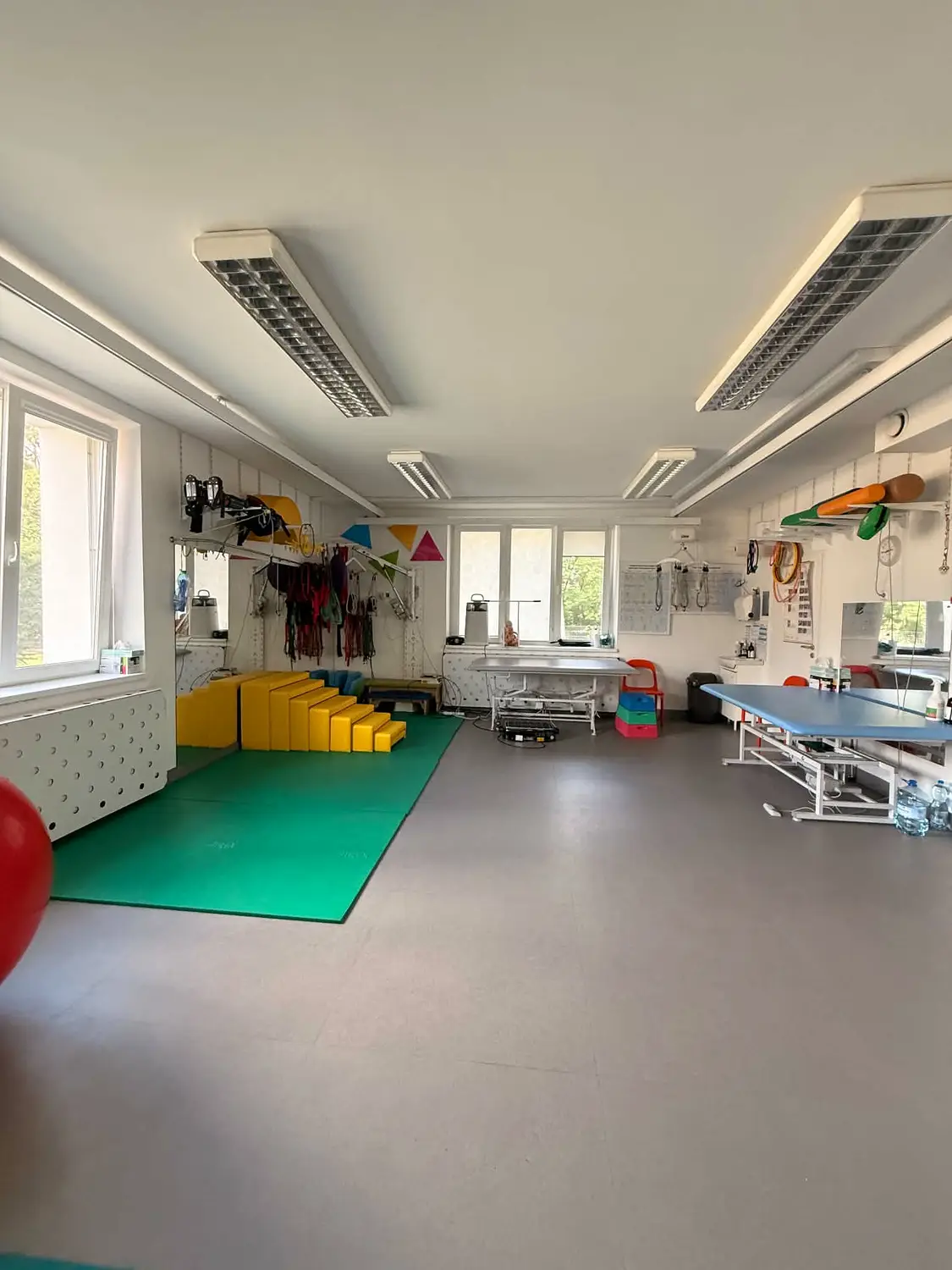 Przestrzeń do rehabilitacji z matą, leżanką i sprzętem do ćwiczeń.